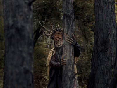 Uhyggelig maskeklædt træmand foran gammelt træ
