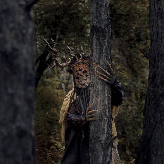 Uhyggelig maskeklædt træmand foran gammelt træ